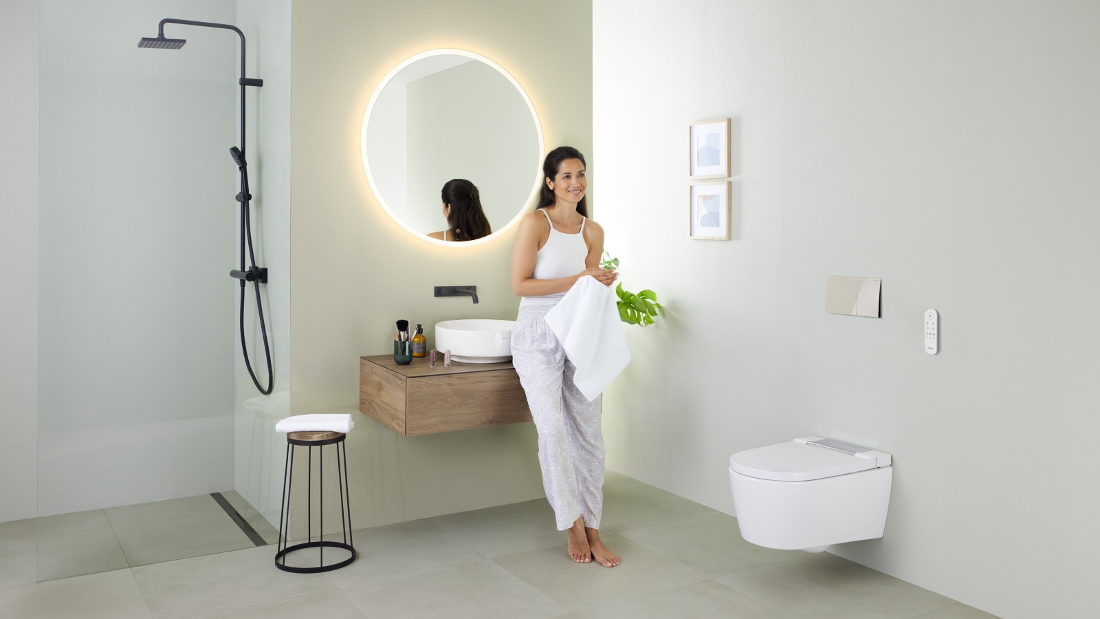 Žena naslonjena na umivaonik u kupaonici s tuš WC-om Geberit AquaClean Sela te umivaonikom i namještajem Geberit VariForm Žena naslonjena na umivaonik u kupaonici s tuš WC-om Geberit AquaClean Sela te umivaonikom i namještajem Geberit VariForm